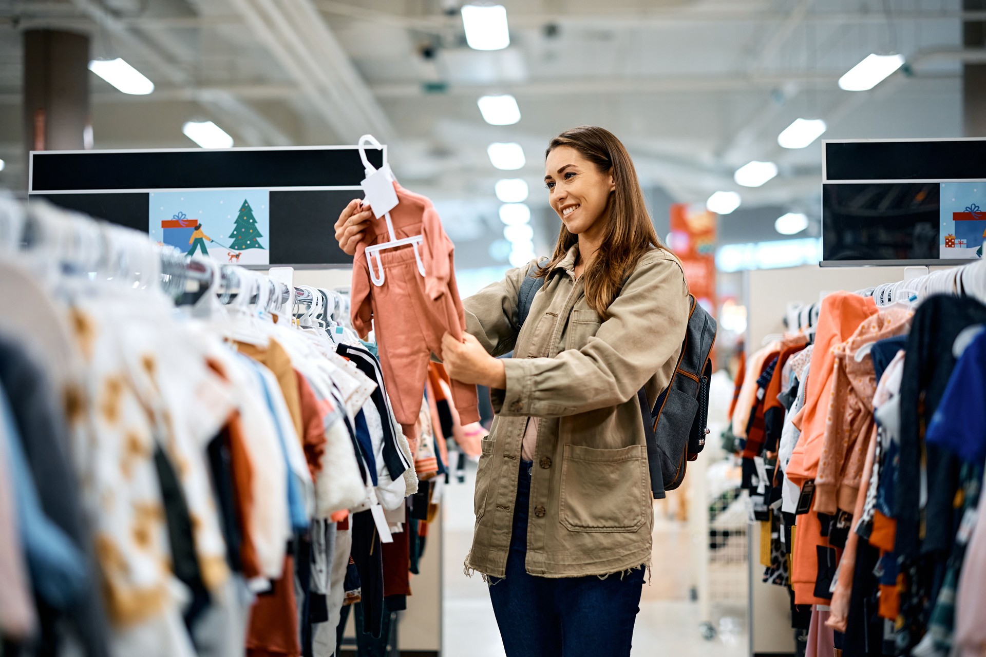 Young happy woman choosing baby clothes at the store.